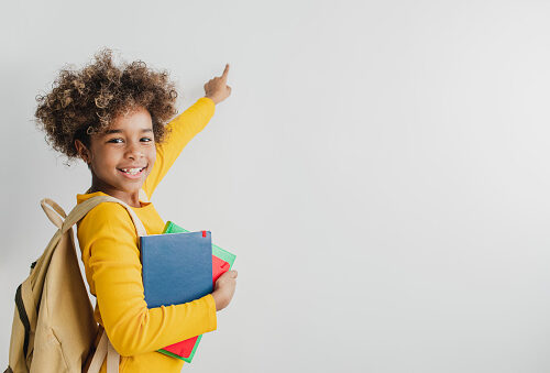 3 A little African American girl is holding books and smiling in front of the white wall
